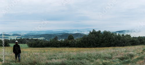 Man standing on meadow with trees looking to misty fog valley. Czech republic