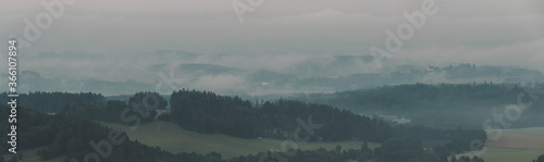Panoramic view to forest, meadow silhouette with misty fog. Czech landscape