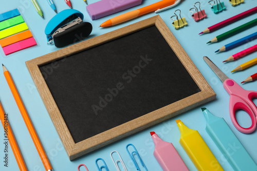 Flat lay with school supplies and empty board on blue background, space for text