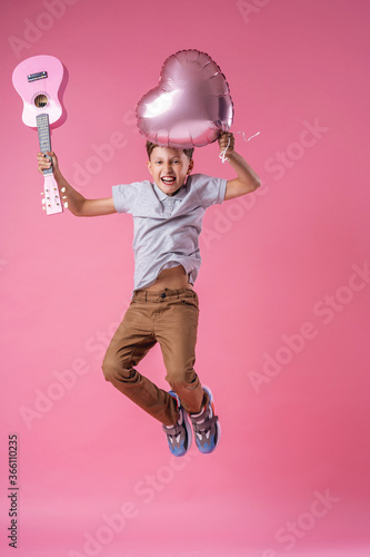 cheerful boy jumps with pink balloon and ukulele gyrator on Valentine's day. photo