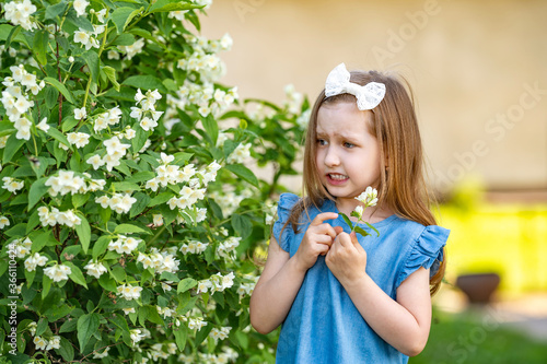 scared little girl 4 years old near a Jasmine Bush, afraid of insects in the garden.