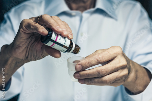 The nurse female hands holding medicine bottle and puts drops in a glass, healthcare concept background with copy space.