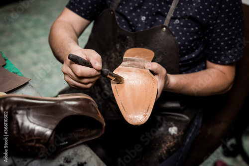 Male cobbler sitting at his shop and repairing man's shoe, brushing glue over sole.  Vintage look.