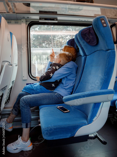 Travel by train. Mother and son go by train. Blue seats in the car. Young mother with child and looking out the window while traveling by train. Poland. Europe.