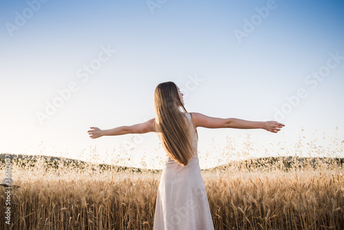 Young woman on her back opens her arms in the field feeling free. Blonde girl with long hair enjoys the summer sun