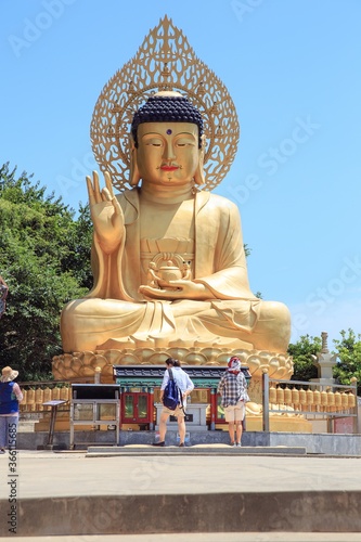 Vertical shot of tourists near large golden Buddha statue at the Sanbanggulsa Temple in Jeju, Korea photo