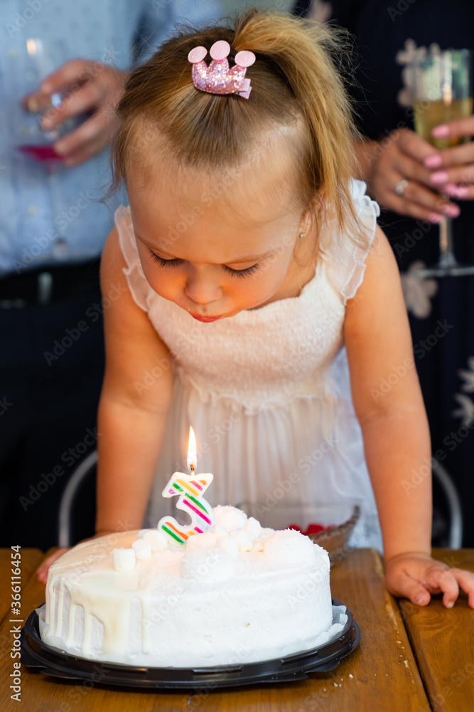 little girl blows out candle on cake of birthday.