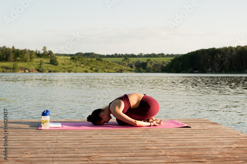 A beautiful girl trains on the river bank. She does yoga exercises, does asanas. By doing stretching, lunges and bends, the girl strengthens the muscles of the press, back and prolongs youth. photo