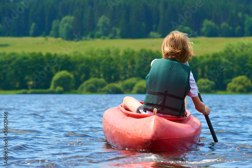 Active happy boy in summer holiday. Teenage school boy having fun enjoying adventurous experience kayaking on lake on a sunny day during summer vacation.
