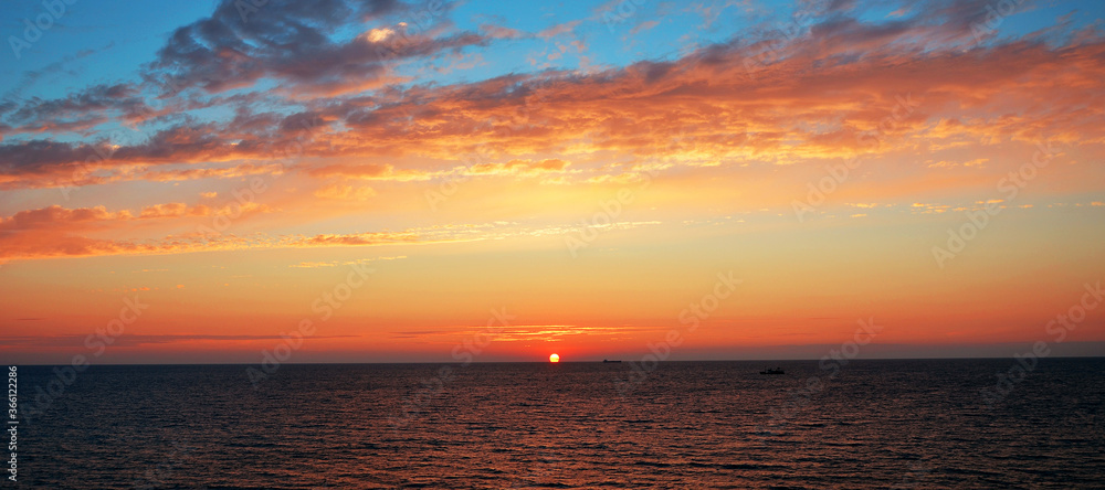 Beautiful sky with orange clouds lit by the sun setting in the sea