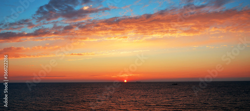 Beautiful sky with orange clouds lit by the sun setting in the sea © Sergey