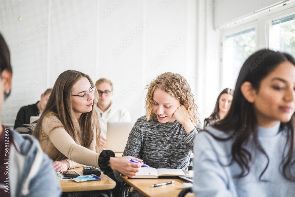 Female students discussing over book at desk in classroom Female students discussing over book at desk in classroom