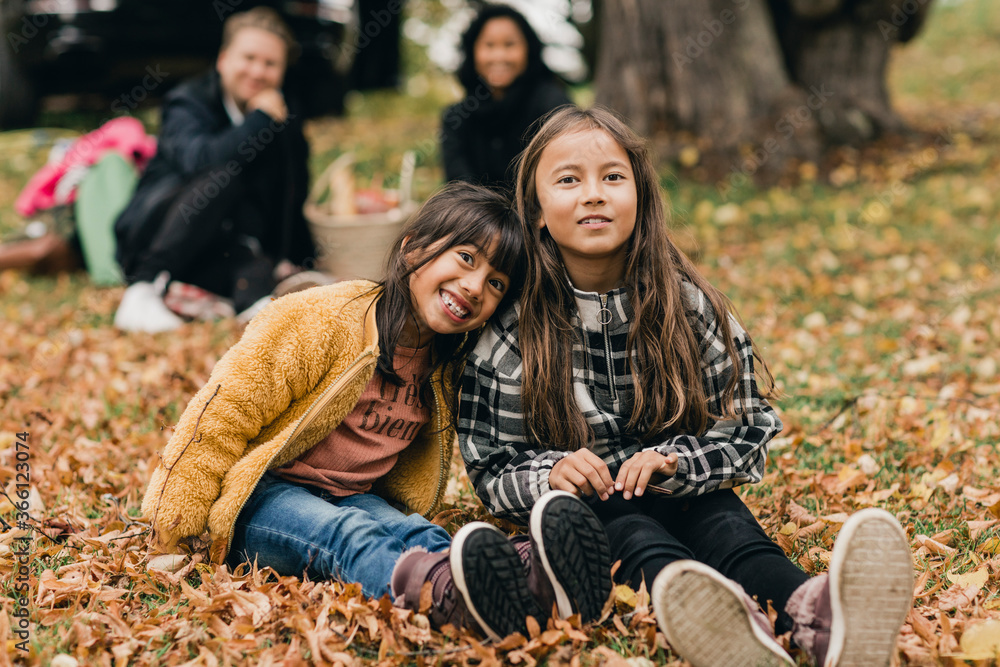Portrait of smiling sisters sitting on autumn leaves during picnic with parents Portrait of smiling sisters sitting on autumn leaves during picnic with parents