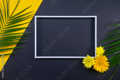 Frame of tropical palm leaves with flowers on black and yellow background