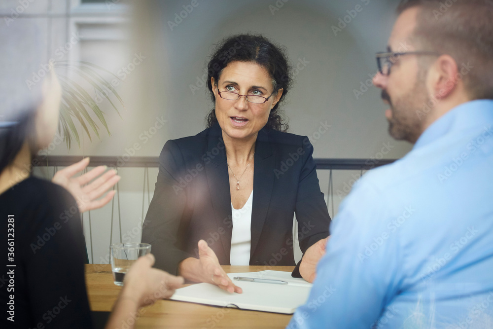 Confident mature female lawyer discussing with businessman and businesswoman during meeting at office Confident mature female lawyer discussing with businessman and businesswoman during meeting at office
