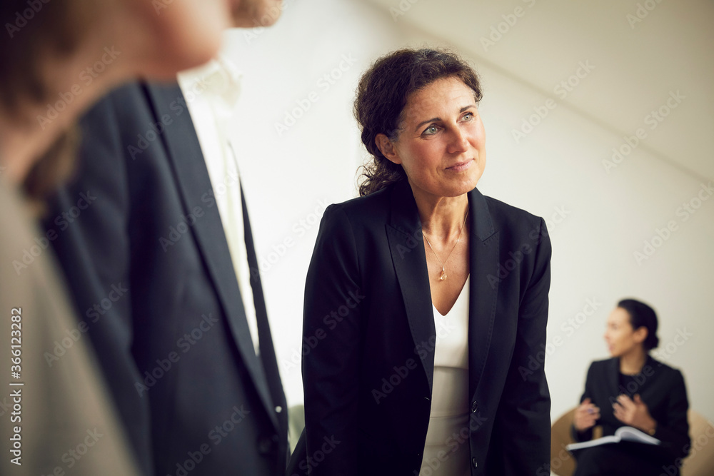 Confident businesswoman looking away while standing with lawyers at office during meeting Confident businesswoman looking away while standing with lawyers at office during meeting