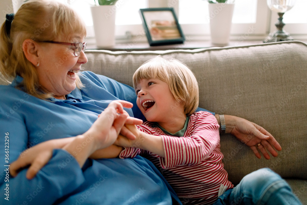 Playful boy with grandmother on sofa in living room at home Playful boy with grandmother on sofa in living room at home