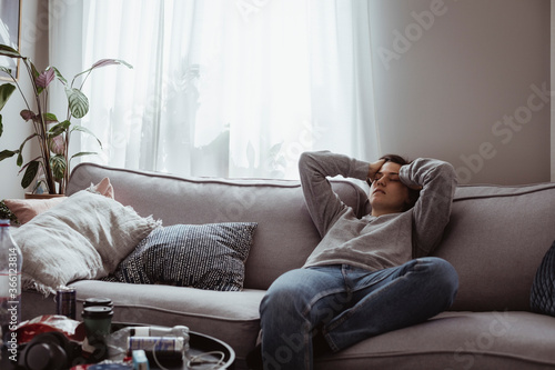Young woman having headache sitting on sofa at home