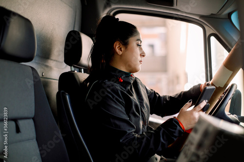 Delivery woman with package using smart phone while driving van photo