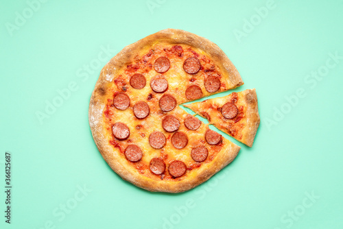 Pepperoni pizza top view on a green background. Sliced pizza above view