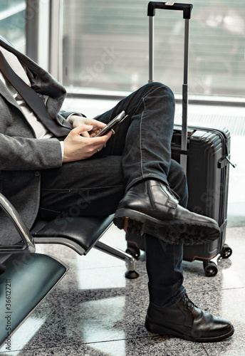 man waiting for his flight at the airport and looking at a mobile phone