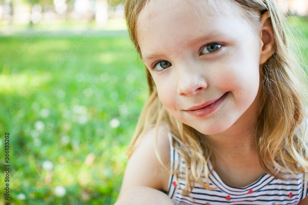 Portrait of a beautiful little girl with loose blond hair on a background of summer greenery. Portrait of a beautiful little girl with loose blond hair on a background of summer greenery.