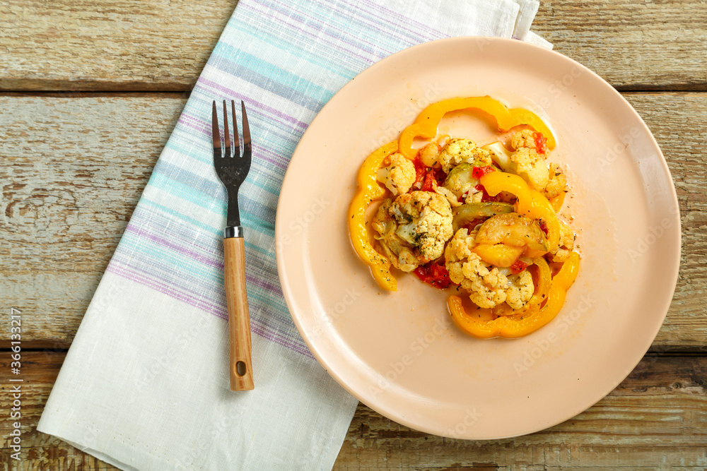 Vegetable stew on a beige plate on a napkin with a fork on a wooden table. Vegetable stew on a beige plate on a napkin with a fork on a wooden table.