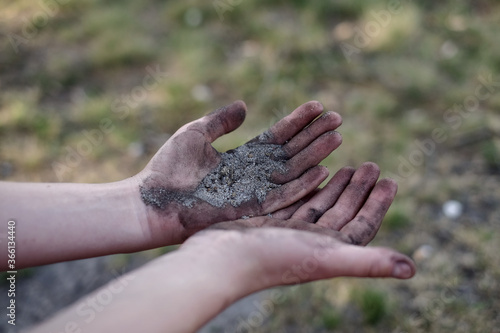 Dreckige Hände vor trockenem Boden mit schwarzem Sand und Staub