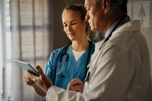 Male doctor discussing patients results on digital tablet with female nurse in scrubs