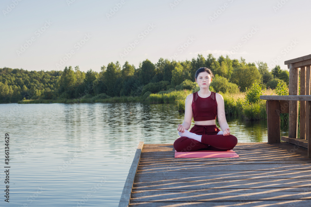 girl doing yoga on wooden pier by lake in summer