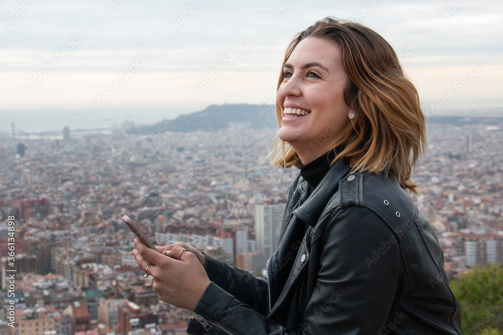 smiling young woman talks on her mobile phone with the city in the background smiling young woman talks on her mobile phone with the city in the background