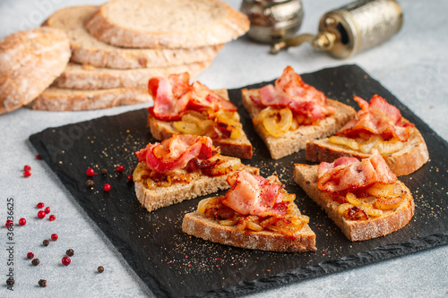 Delicious whole-grain bread sandwiches with fried onions, bacon and freshly ground pepper. Gourmet appetizer. Selective focus