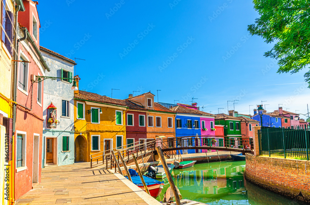 Colorful houses of Burano island. Multicolored buildings on fondamenta embankment of narrow water canal with fishing boats and wooden bridge, Venice Province, Veneto Region, Northern Italy
