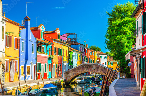 Colorful houses of Burano island. Multicolored buildings on fondamenta embankment of narrow water canal with fishing boats and stone bridge, Venice Province, Veneto Region, Italy. Burano postcard photo