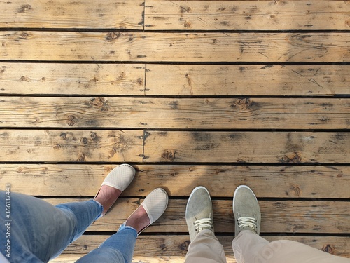 Two people are standing on a wooden surface. Top view of feet shod in light summer shoes