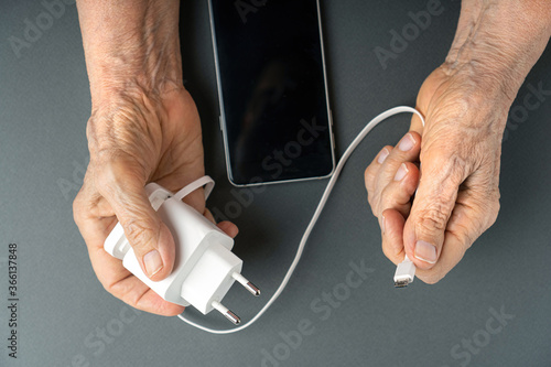 Old woman wrinkled hands holding a charger for smartphone. Elderly people and modern technologies concept.