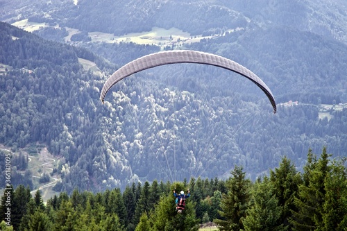 Paragliding among the mountains on sunny summer day. Paraglider flight against beautiful mountains landscape and bright sky. Parachuting in the mountains. Human flying high in the sky. Freedom concept