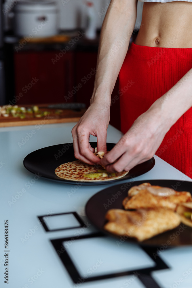 Woman's hand decorates pancakes with a fruits kiwi and banana. Black plate, white table