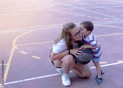 young girl helping a little boy play basketball and the boy gives her a kiss as a thank you