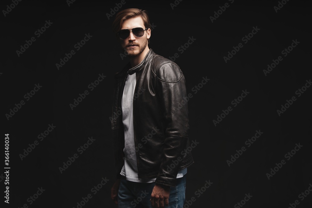 Fashion man, Handsome serious beauty male model portrait wear sunglasses and leather jacket, young guy over black background