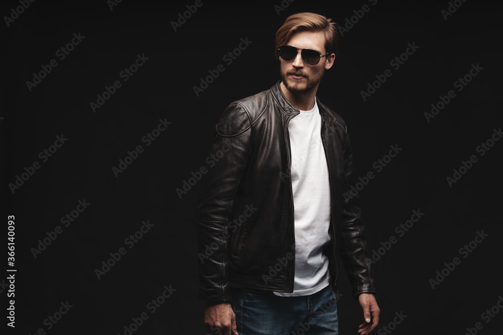 Fashion man, Handsome serious beauty male model portrait wear sunglasses and leather jacket, young guy over black background Fashion man, Handsome serious beauty male model portrait wear sunglasses and leather jacket, young guy over black background