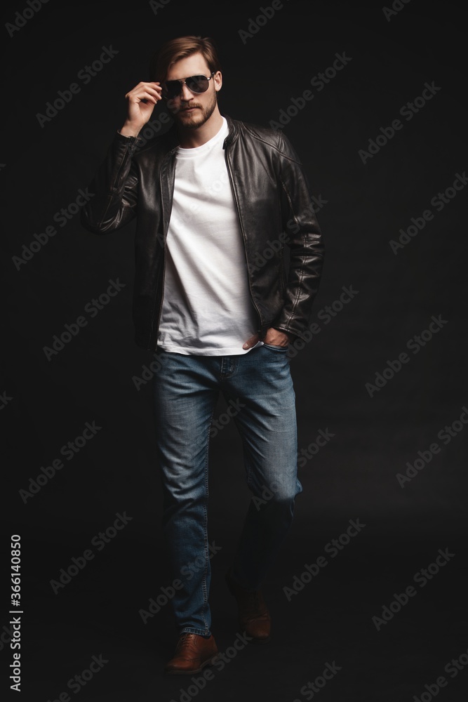 Fashion man, Handsome serious beauty male model portrait wear sunglasses and leather jacket, young guy over black background Fashion man, Handsome serious beauty male model portrait wear sunglasses and leather jacket, young guy over black background