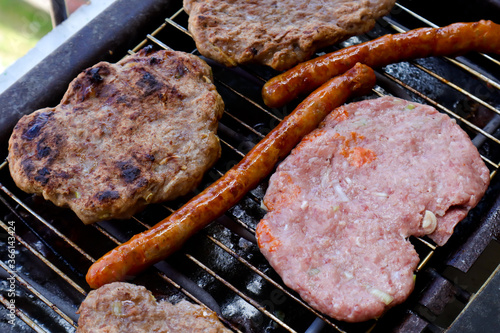 Traditional serbian barbecue (rostilj)  homemade sausages and burgers. Preparing a barbecue on a grill, outdoor roasting meat. Traditional Balkan cuisine, close up, top view  photo