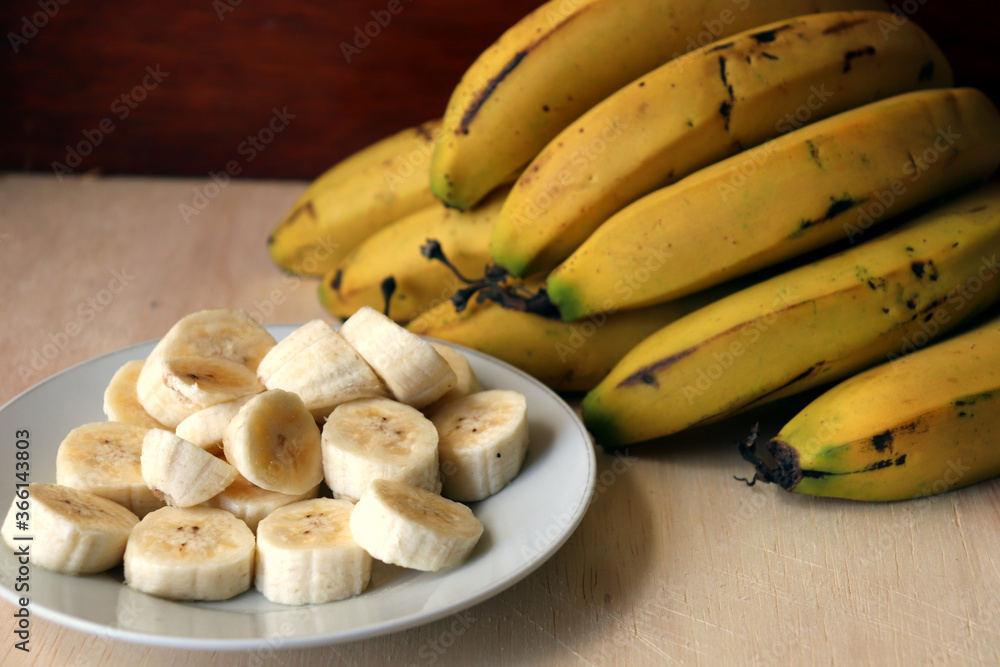 Banana slices on a white dish and bananas fruit in the background. Banana slices on a white dish and bananas fruit in the background.