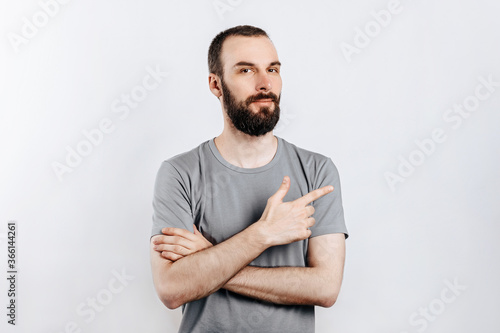 Handsome brunette man with a beard points a finger at a place for advertising on a white background