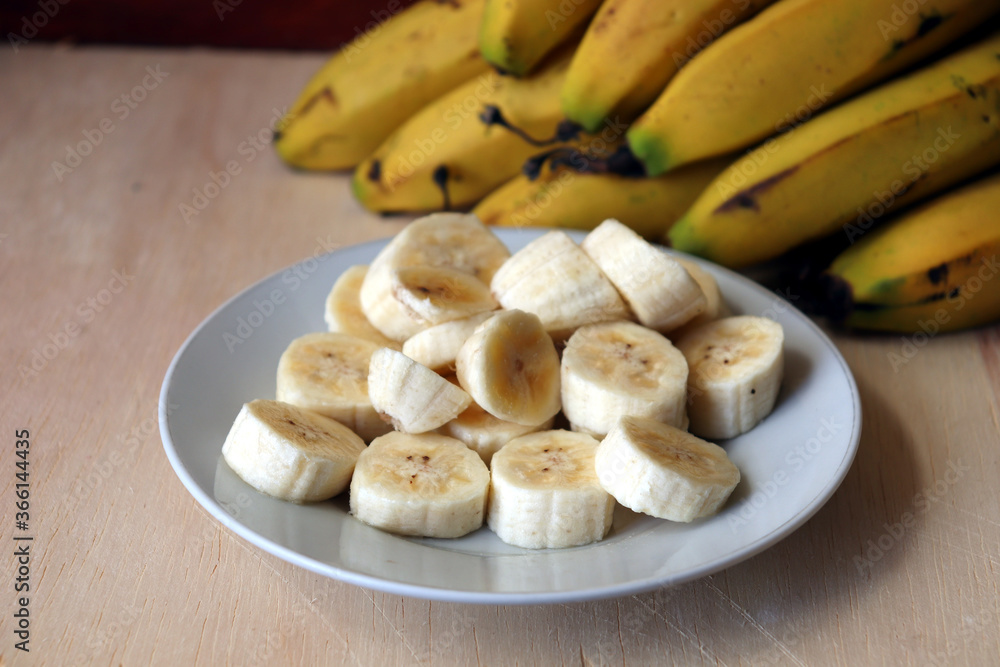 Banana slices on a white dish and bananas fruit in the background. Banana slices on a white dish and bananas fruit in the background.