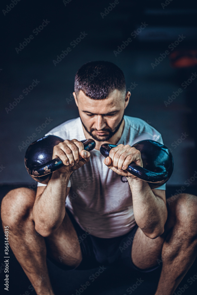 Bearded fitness man doing a weight training by lifting heavy kettlebell. Yong athlete doing kettlebell swings. Bodybuilder lifting with kettlebell.