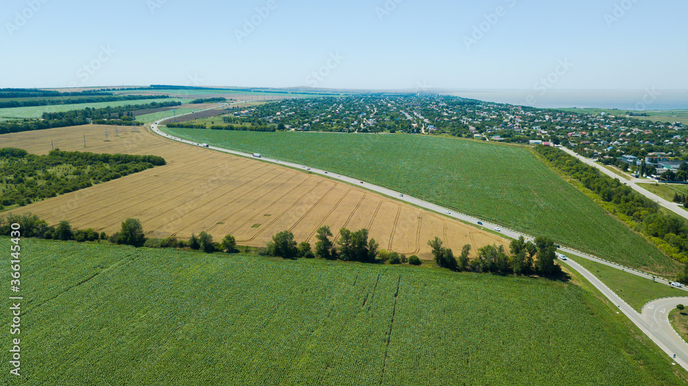 Aerial view of turn highway road between meadow and agricultural field.