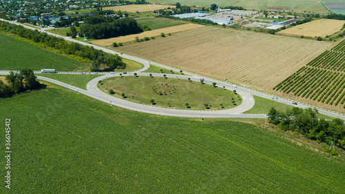Aerial view of highway traffic circle between meadow and agricultural field.