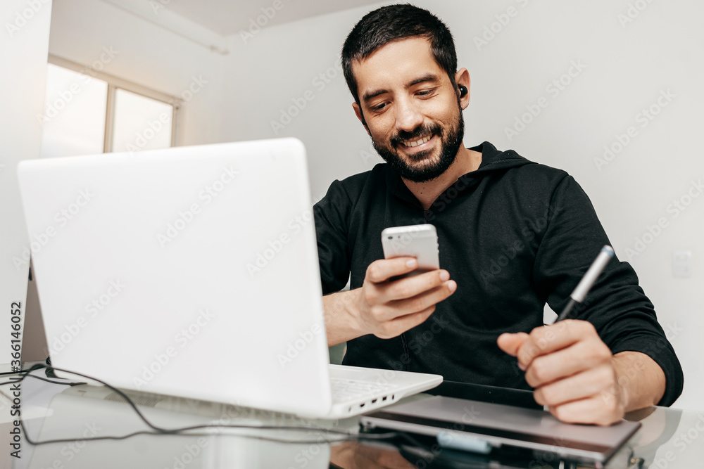 Designer working from home using laptop and tablet. Checking something on the phone Designer working from home using laptop and tablet. Checking something on the phone